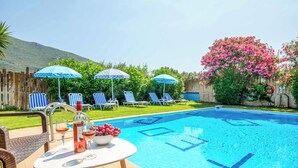 A swimming pool with lounge chairs and umbrellas, a table with drinks and a bottle, and a flower bush. - Villa Teo - Four Bedroom Villa, Sleeps 8 (Ionian Islands)