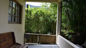 Un balcon avec un banc en bois, une vue sur une végétation luxuriante et une clôture en bambou.