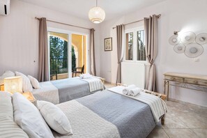 Hotellihuone, jossa on kaksi sänkyä, ikkuna verhoilla, seinään kiinnitetty valaisin ja pieni pöytä, jossa on lamppu.