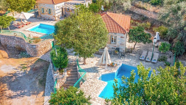 Una villa con dos piscinas, arquitectura de piedra y un jardín.