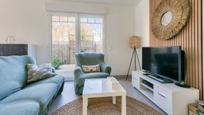 Ein Wohnzimmer mit Sofa, Sesseln, Couchtisch, Fernseher und einem großen Spiegel an der Wand.