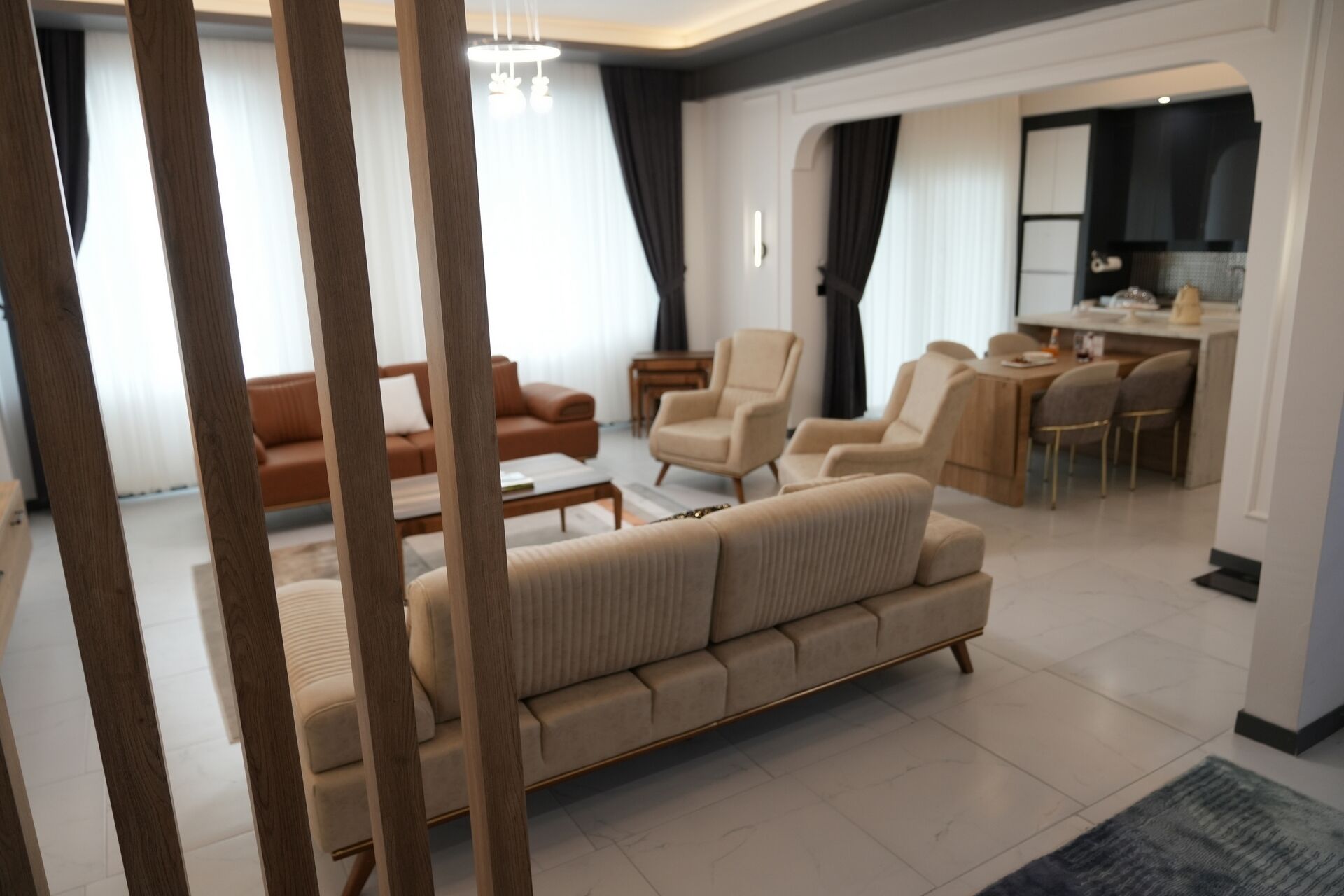Een moderne woonkamer met een beige bank, een eethoek met tafel en stoelen, en een keuken op de achtergrond.