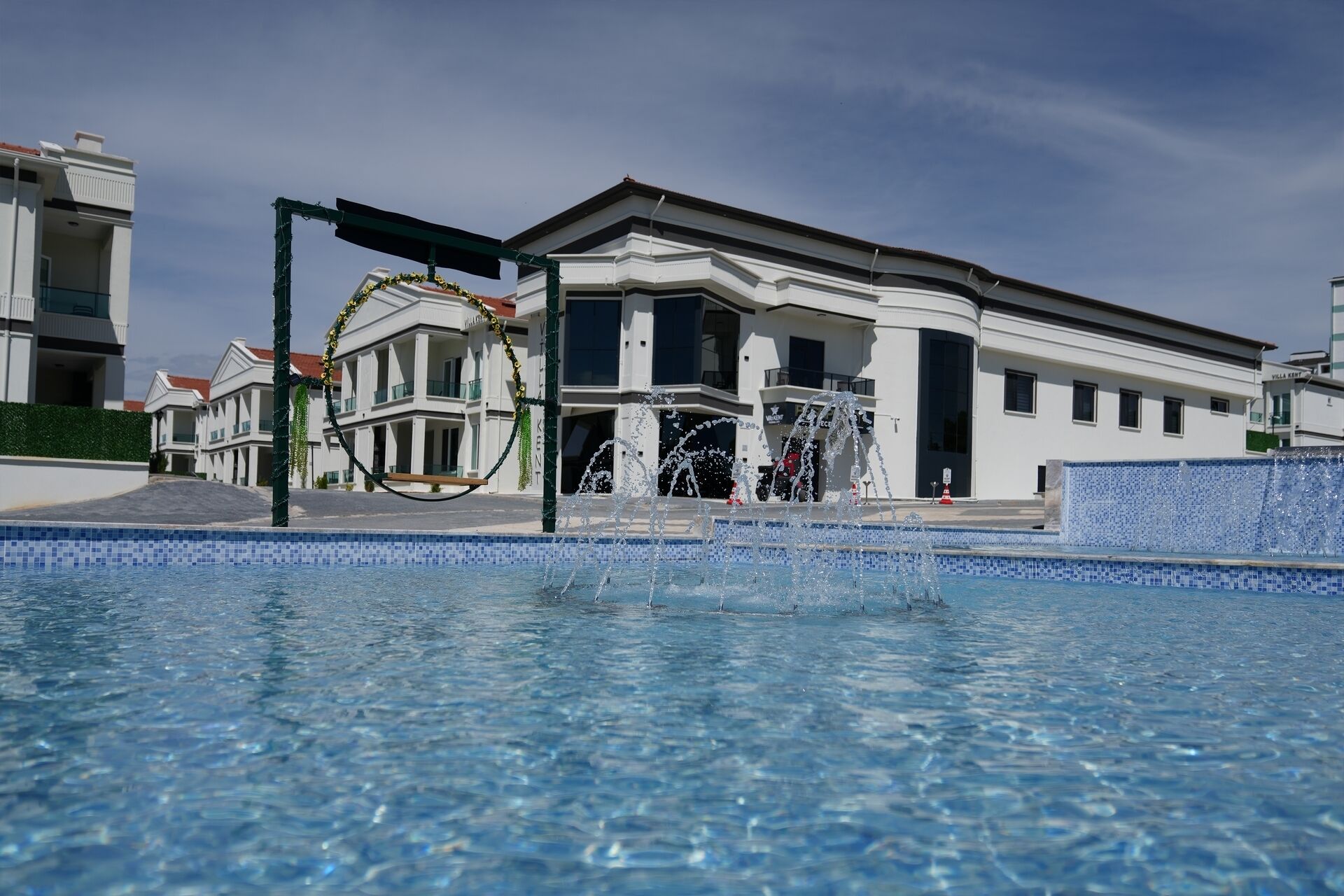 A modern hotel with a swimming pool, a fountain, and a well-maintained garden area.