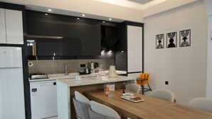 A modern kitchen with a central island, white appliances, and a dining area with a wooden table and grey chairs. - Villa Kent Termal Otel (Ihsaniye)