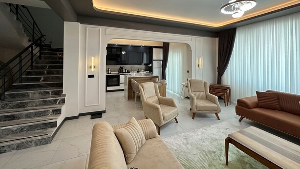 A spacious living room with a sofa, armchairs, and a coffee table. A staircase leads to a kitchen area with modern appliances. - Villa Kent Termal Otel (Ihsaniye)