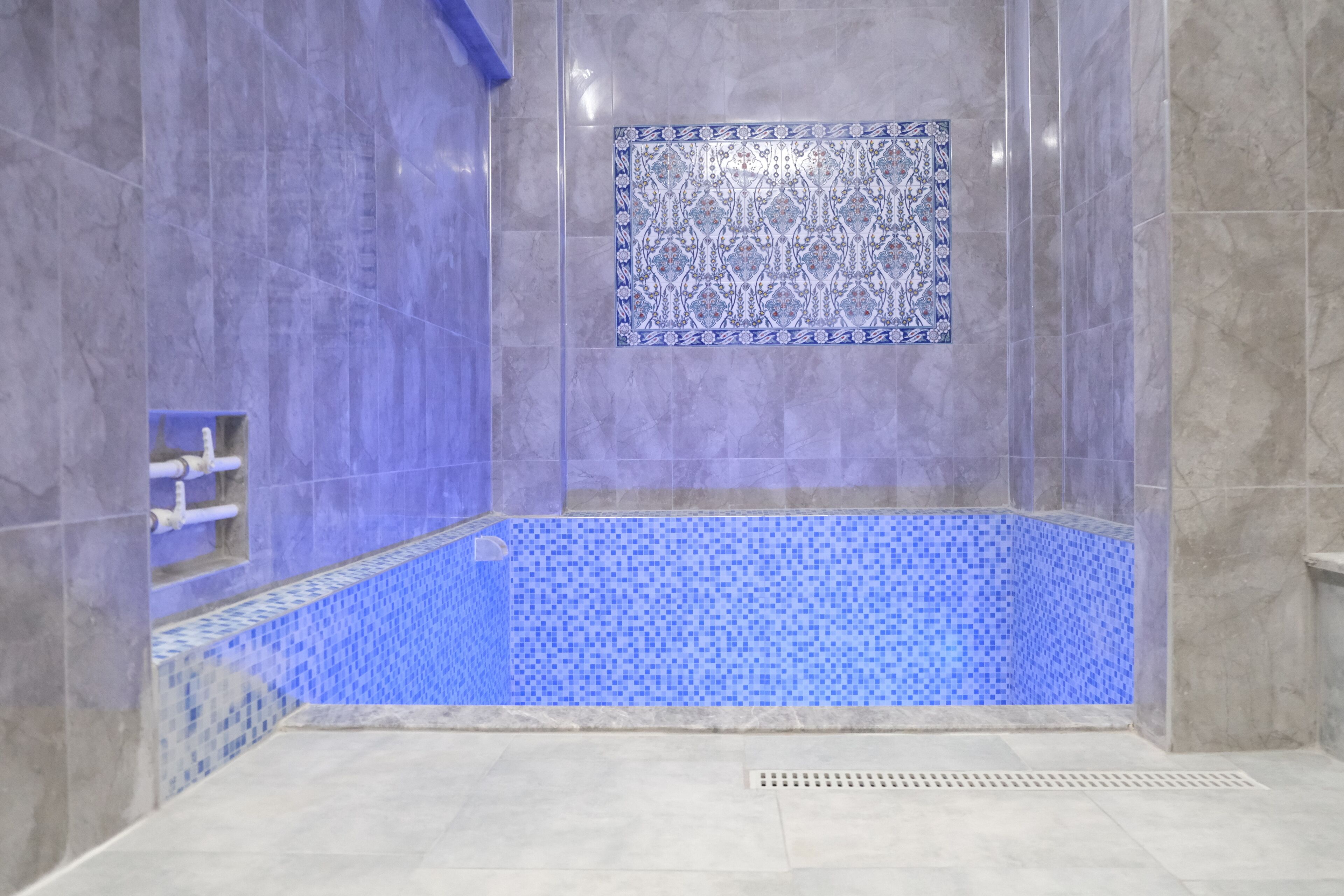 Un baño con piso de baldosas, zona de ducha y pared decorada con azulejos.