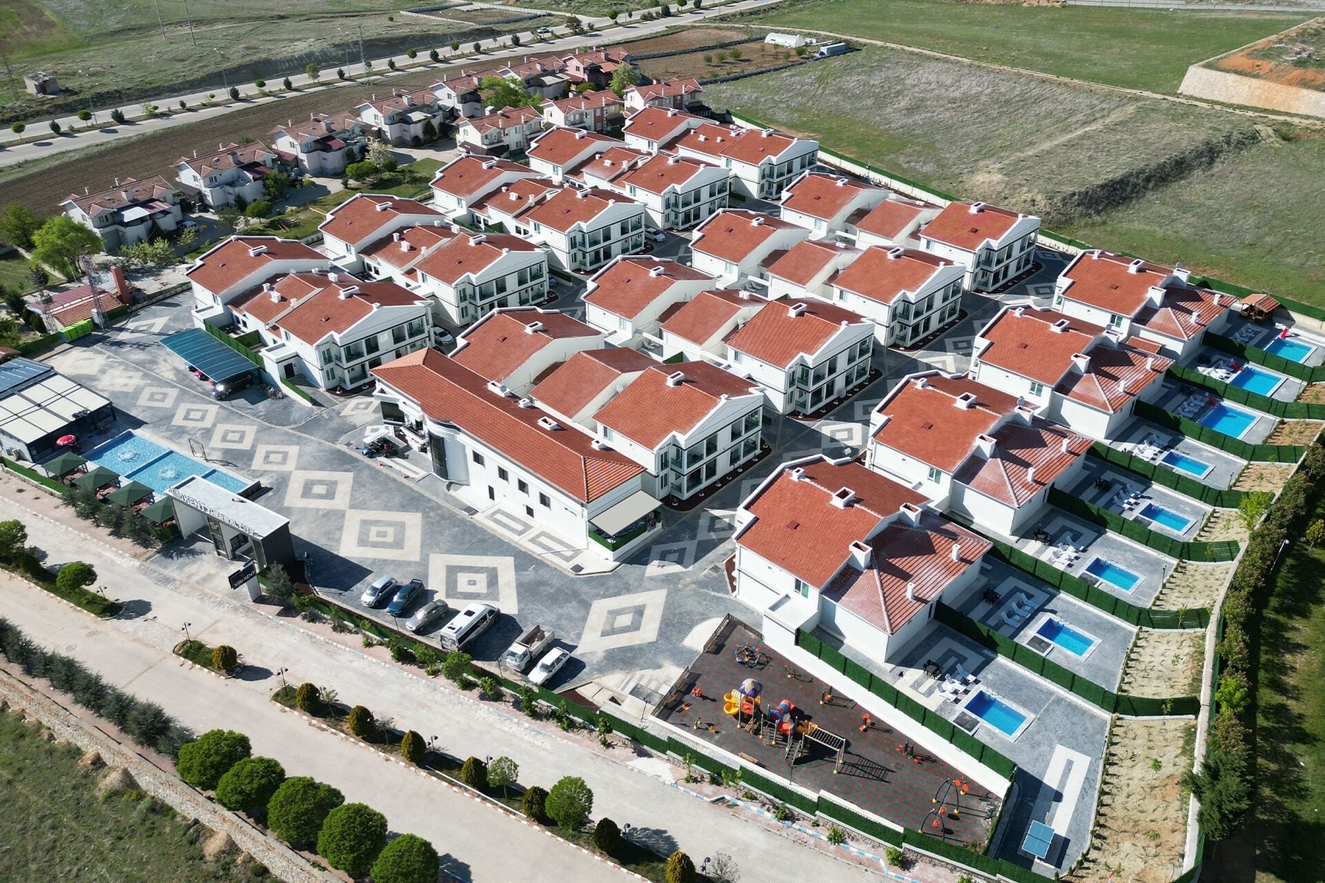 Vista aérea de um complexo residencial com várias casas, uma área de estacionamento central e algumas piscinas.