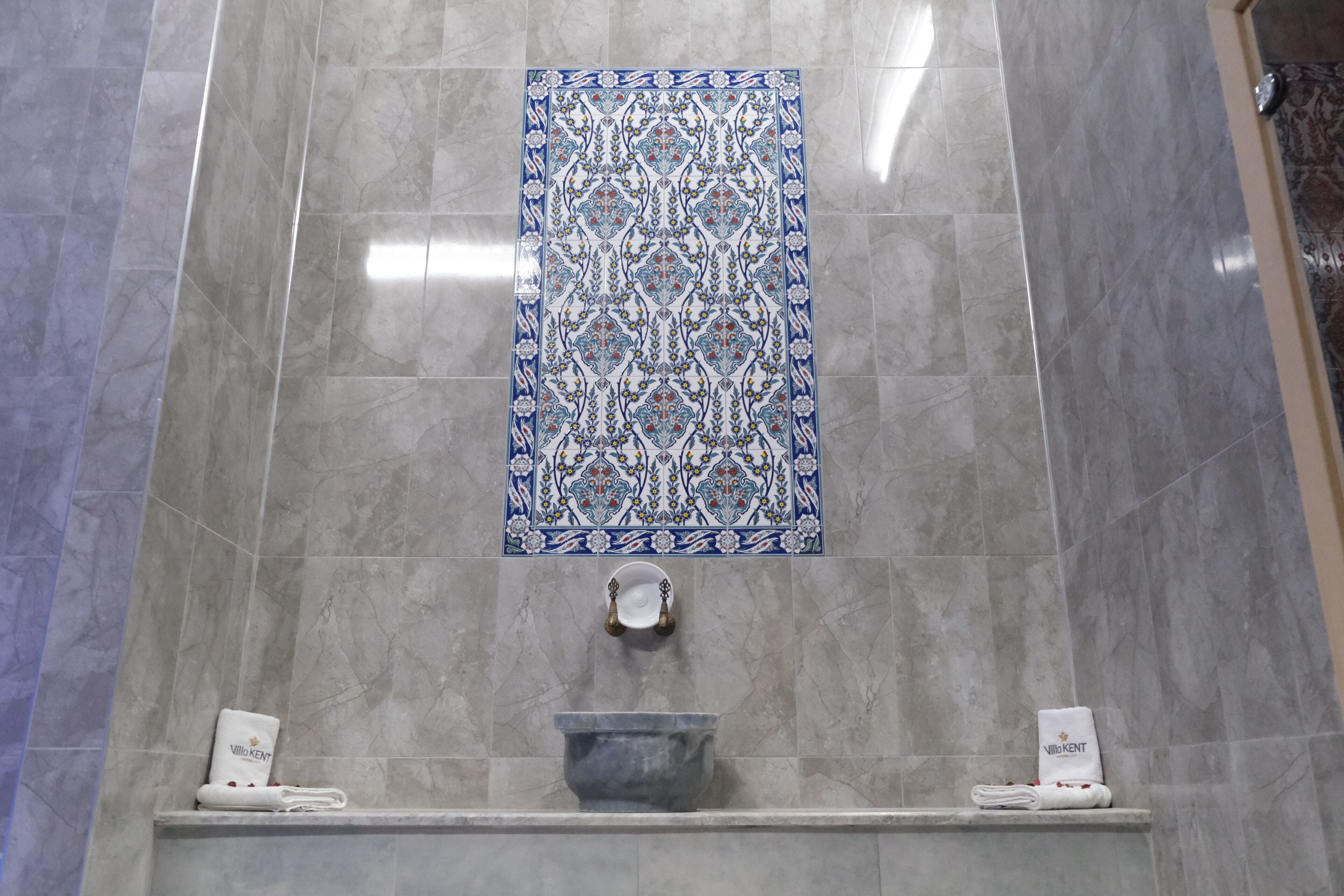 A bathroom with a patterned tile backsplash, a sink, and two towel racks with towels.