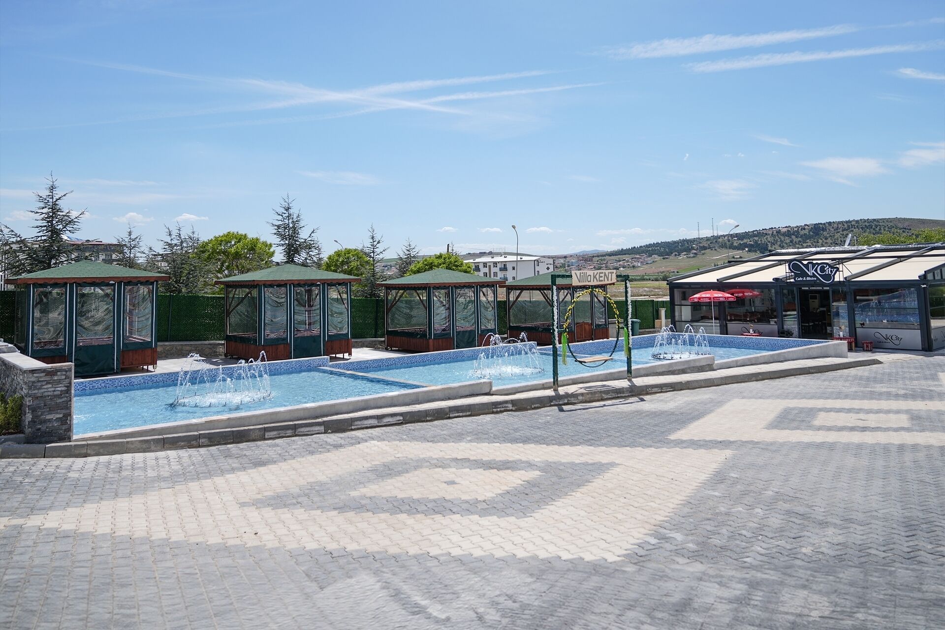 A swimming pool area with three gazebos, a water fountain, and a building labeled "Villa Kent".