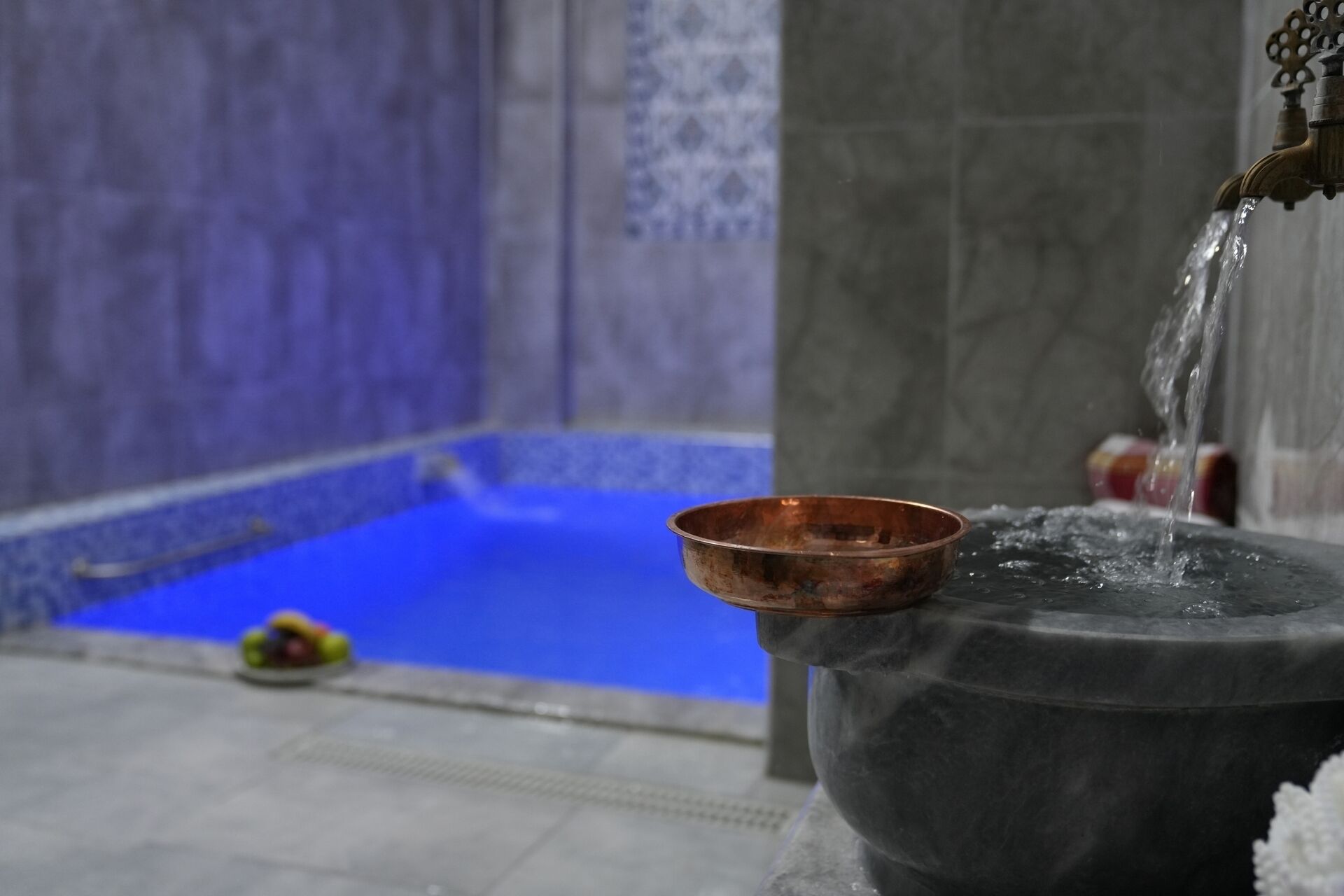 A copper bowl on a stone pedestal with water flowing from a tap.