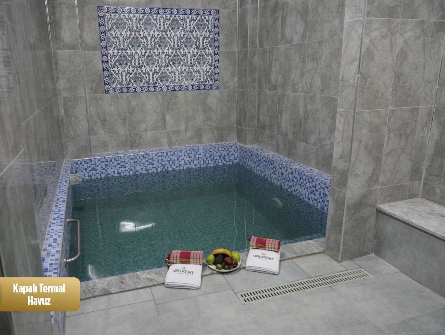 Ein 3x3 Meter großes Whirlpool mit blauem Mosaikrand, ein Handtuch und eine Obstschale auf dem Boden.