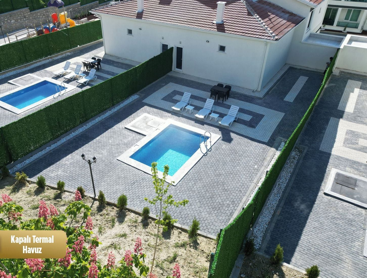 A rooftop swimming pool area with two pools, a covered seating area, and a small building.