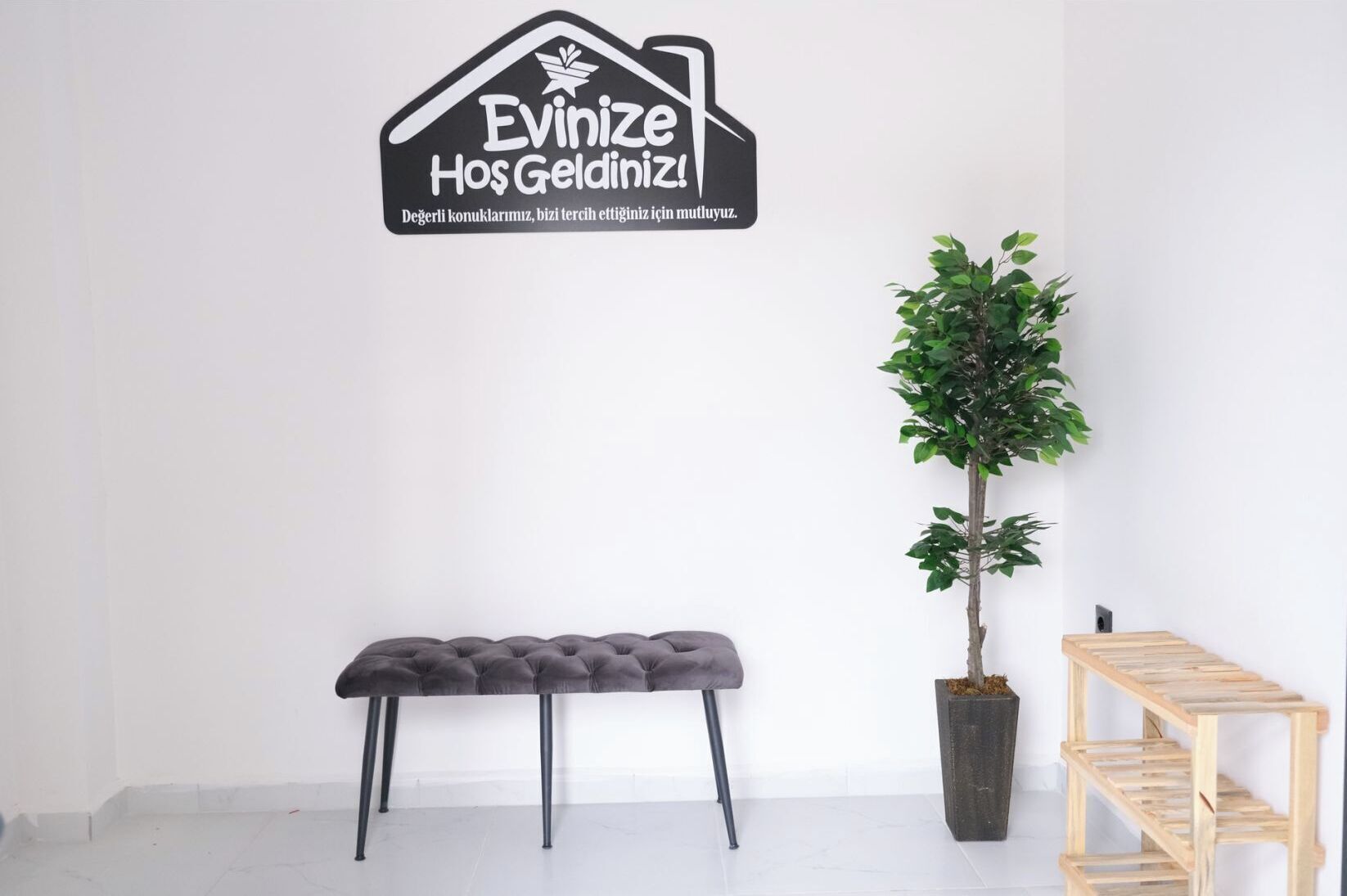 Um quarto com uma placa preta fixada na parede, um banco cinzento, uma planta em vaso e uma prateleira de madeira.