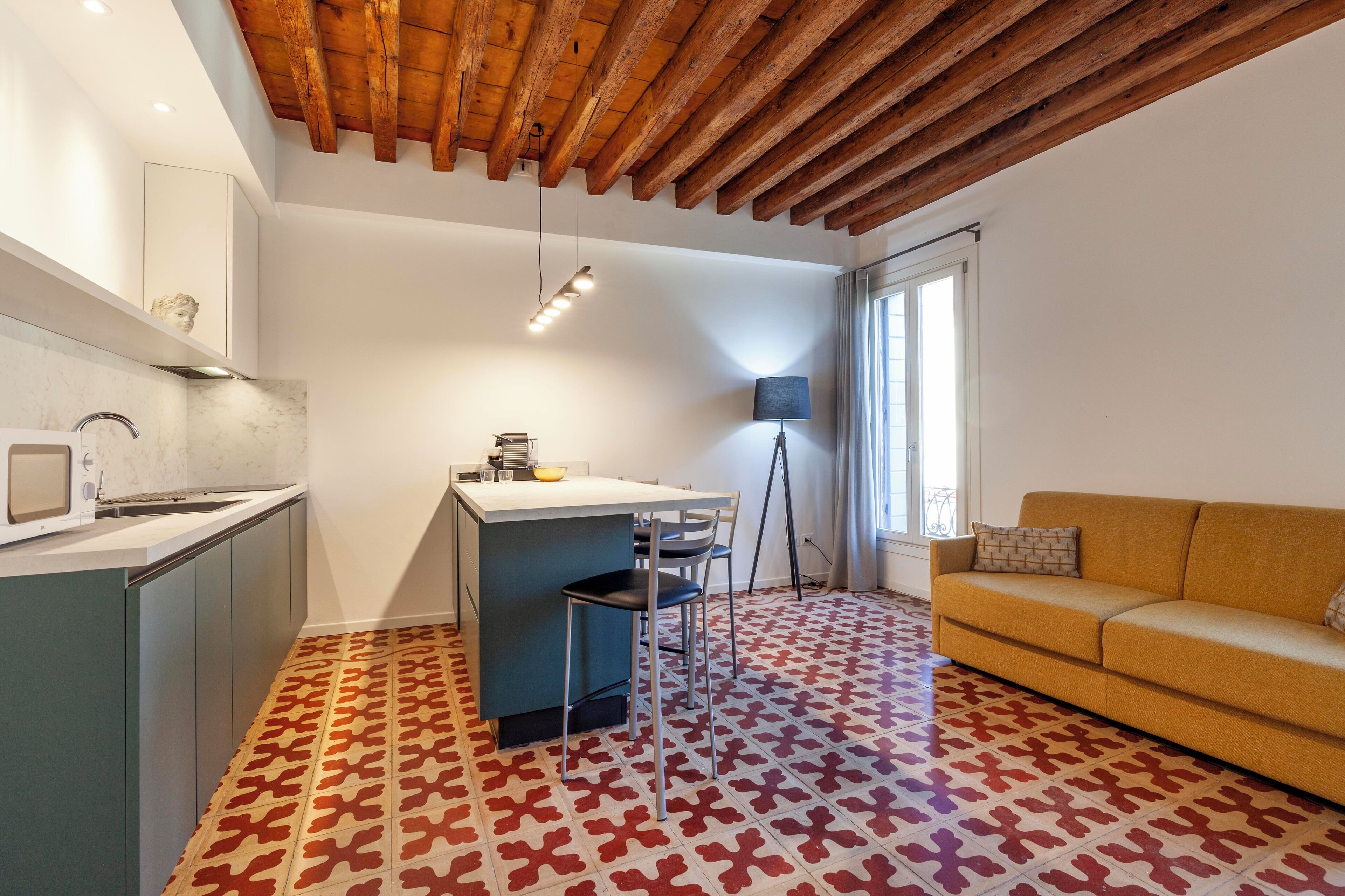 A modern kitchen with a marble countertop, a dining area with a table and chairs, a sofa, and a patterned floor.