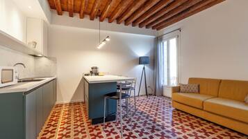 A modern kitchen with a marble countertop, a dining area with a table and chairs, a sofa, and a patterned floor.