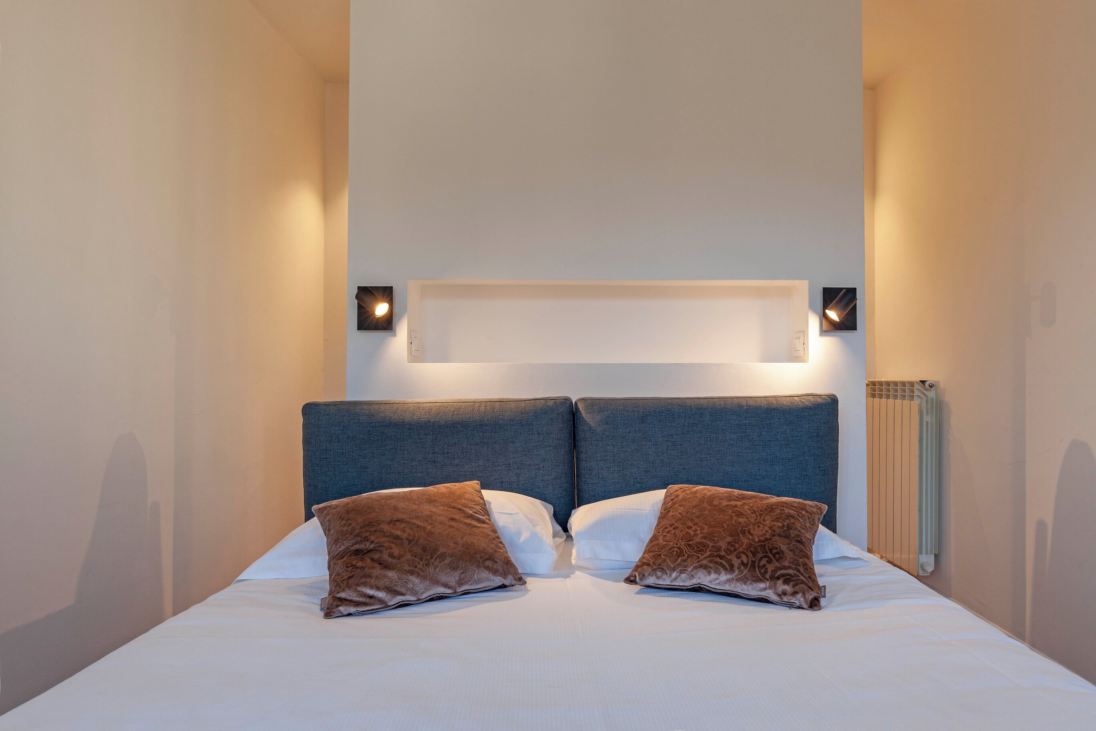 A neatly made bed with two pillows and a headboard with built-in lighting.