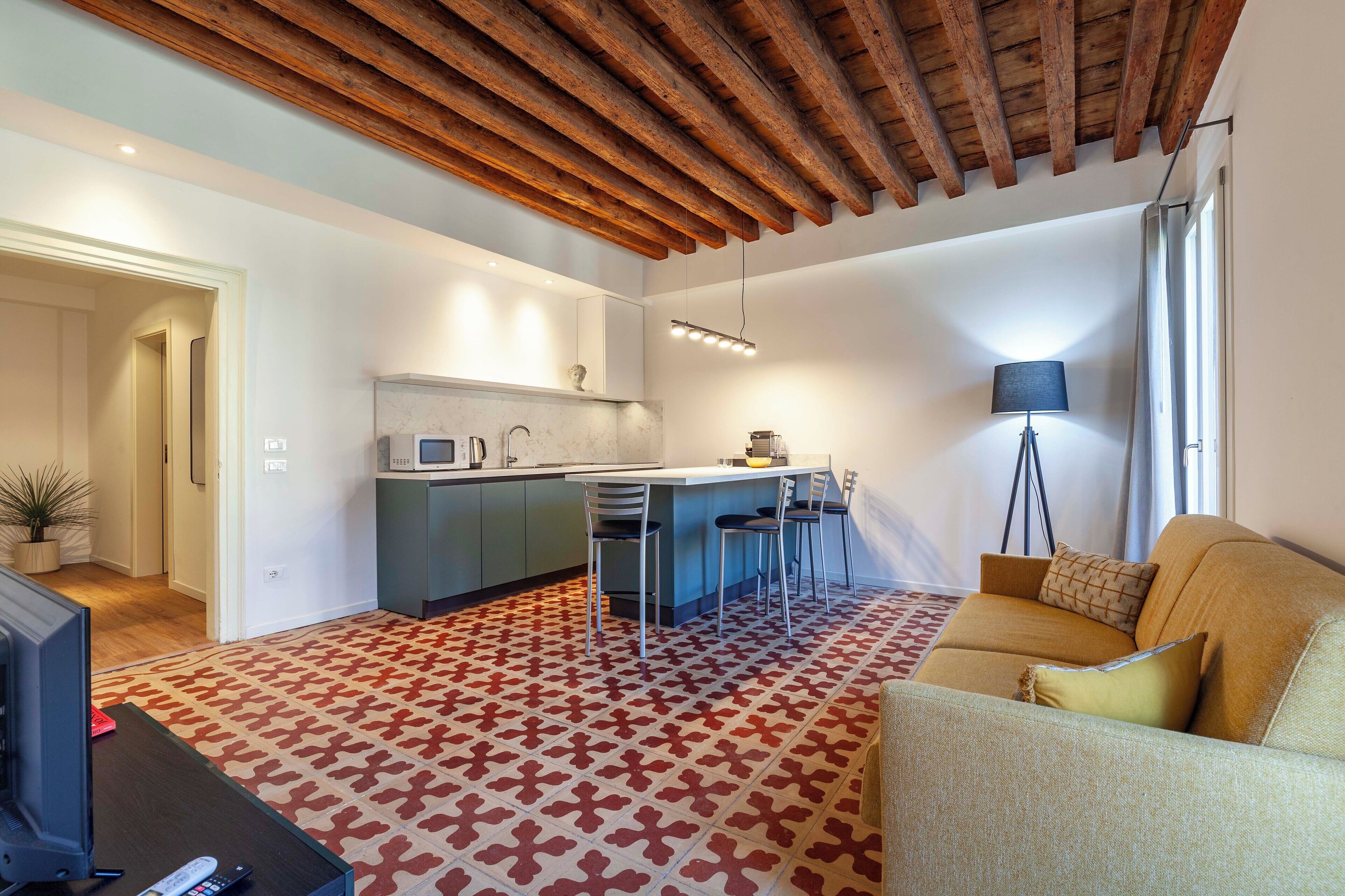 A modern living room with a sofa, a coffee table, and a TV. There is a kitchen area with a dining table and chairs.