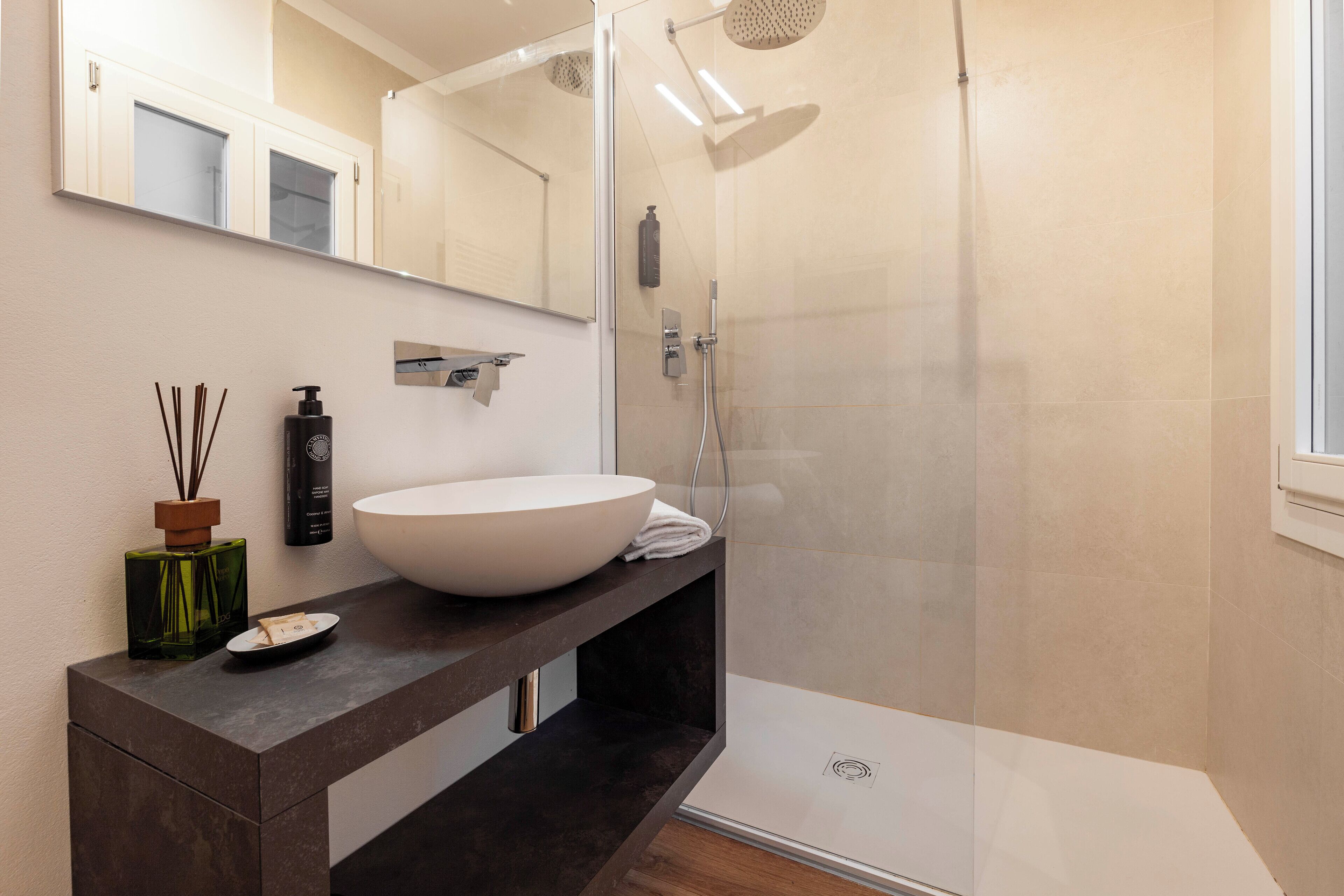 Ein modernes Badezimmer mit einem großen weißen Waschbecken, einem dunklen Holz-Waschtisch, einer Glasdusche und einem Spiegel über dem Waschbecken.