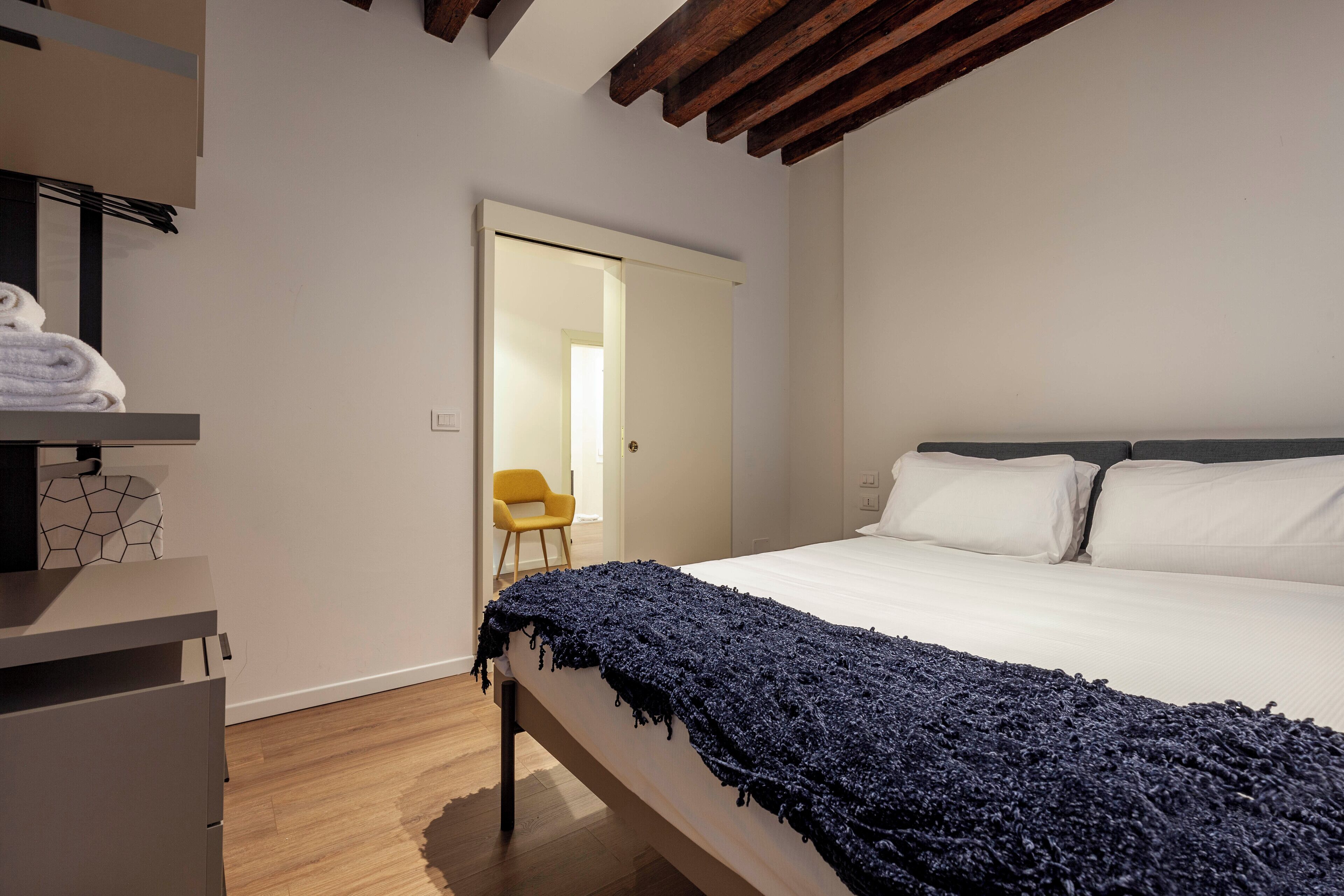 A bedroom with a bed, a bedside table, a chair, and a wardrobe.