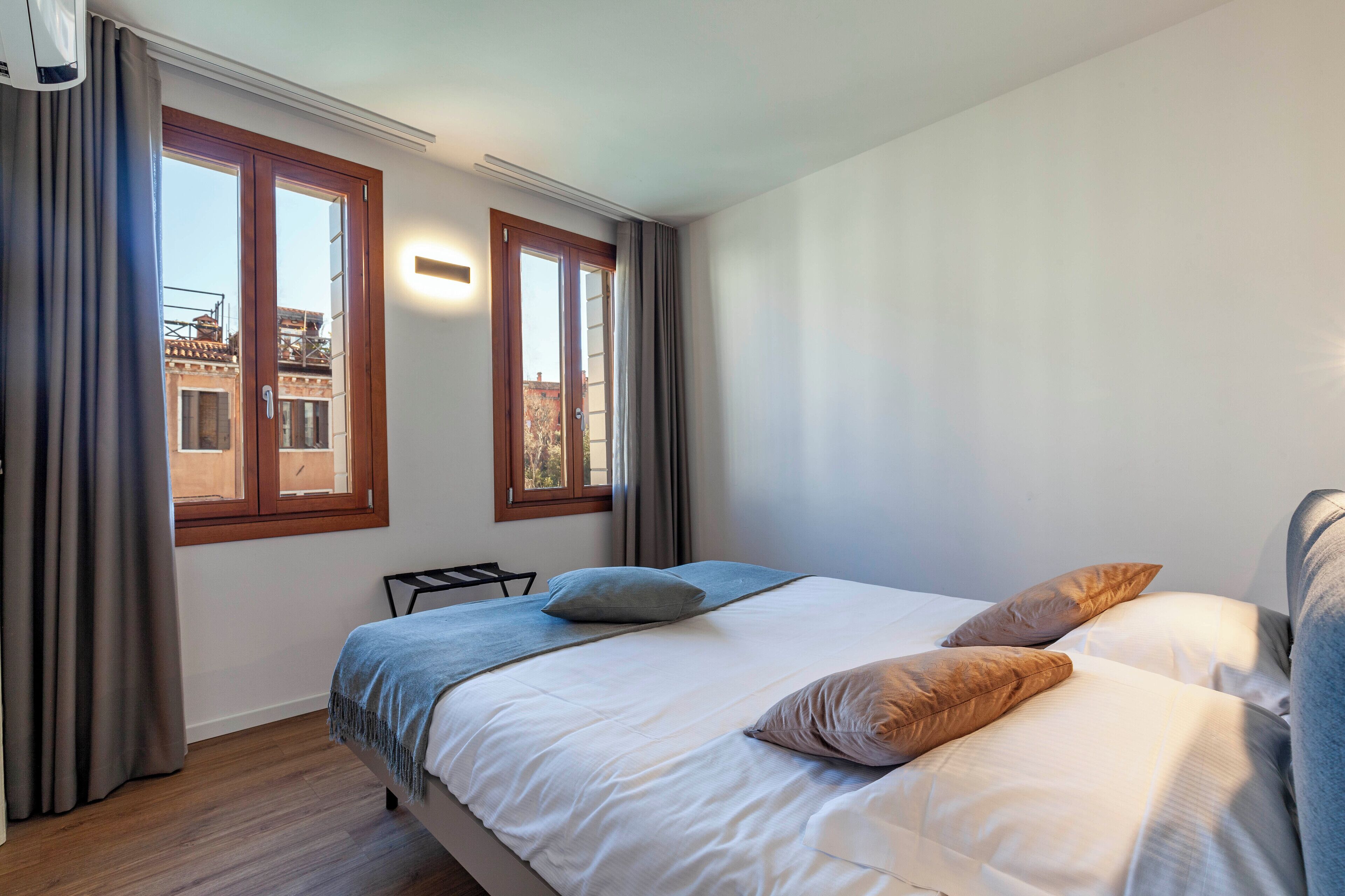 A bedroom with a bed, two pillows, a bedside table, and a window with curtains.