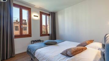 A bedroom with a bed, two pillows, a bedside table, and a window with curtains.