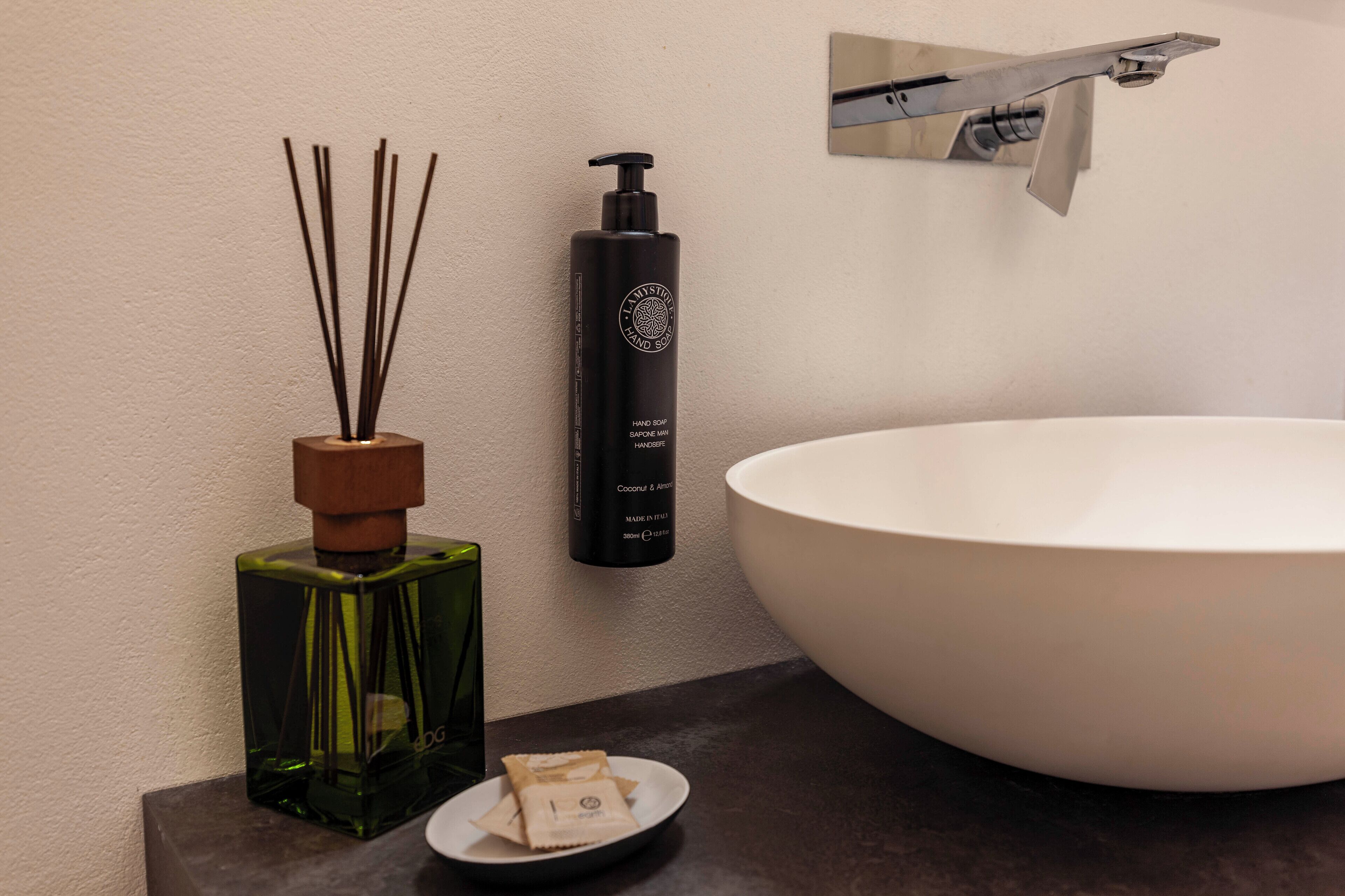 A bathroom with a large white sink, a green bottle of hand soap, and a diffuser with reed sticks.