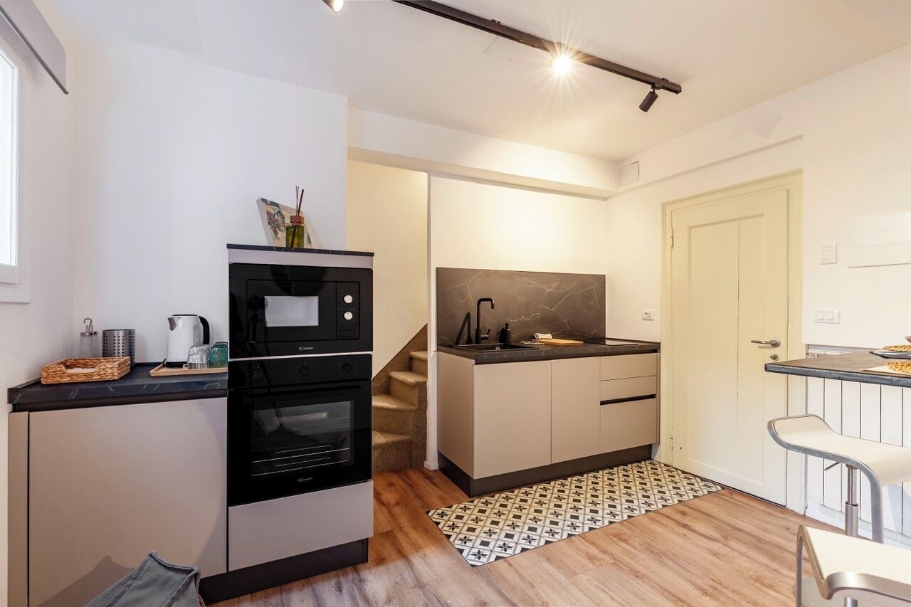 A compact kitchen with a built-in oven, a microwave, and a sink. There is a staircase leading to another level, and a small dining area with a bench.