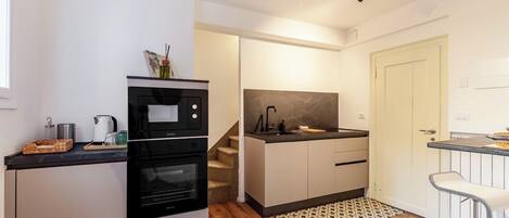 A compact kitchen with a built-in oven, a microwave, and a sink. There is a staircase leading to another level, and a small dining area with a bench.