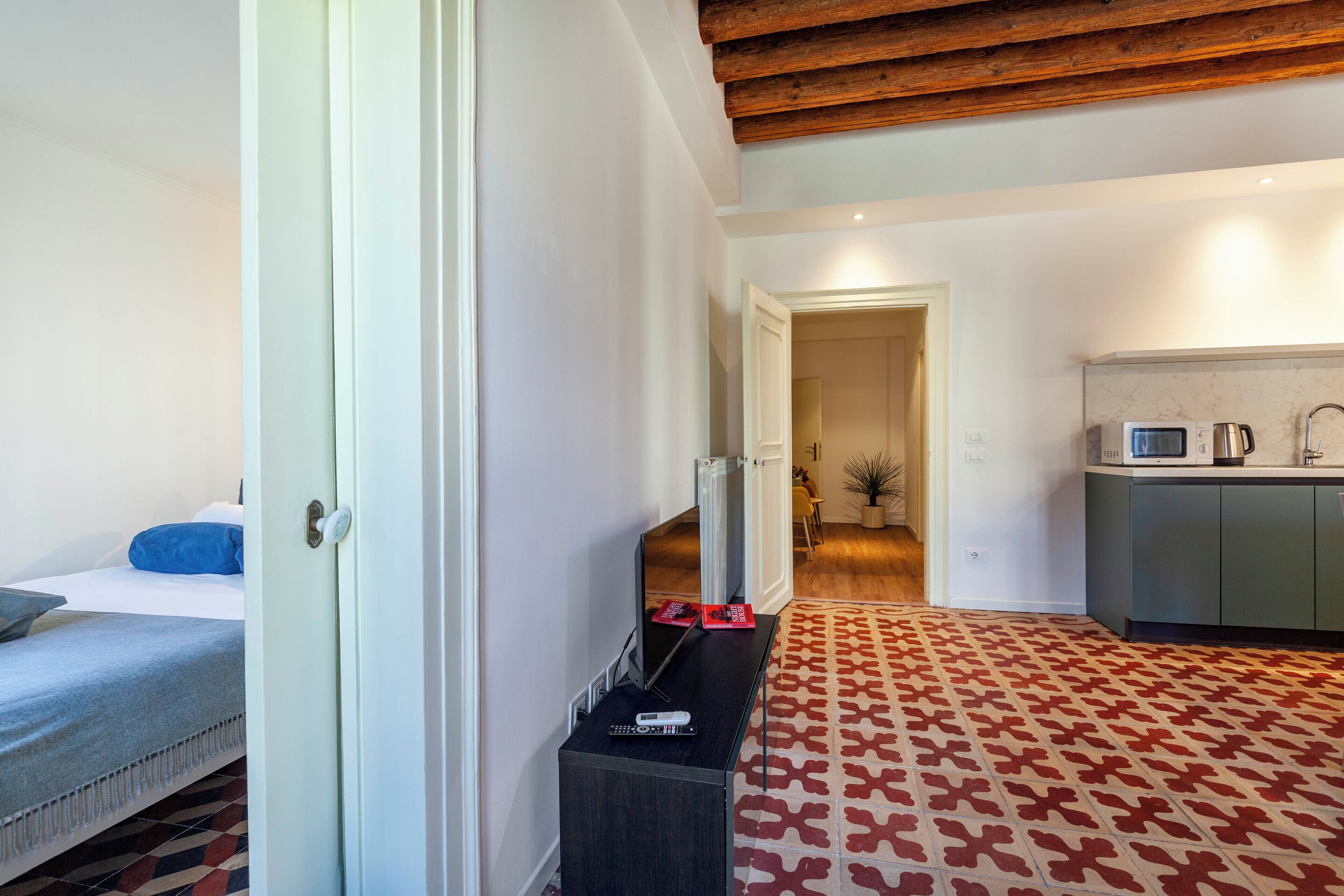 Een hotelkamer met een bed, een televisie, een klein tafeltje met een afstandsbediening en een kamerkleed met een patroon.