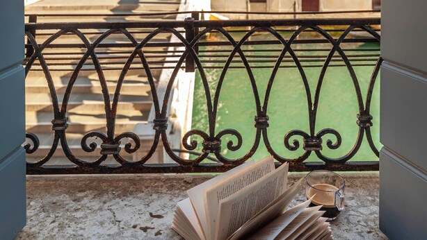 Un balcon donnant sur un pont et des immeubles, un livre et un verre d’eau.