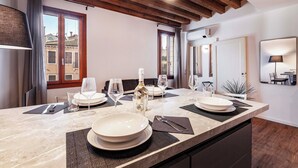 Un coin repas avec une table en marbre dressée pour quatre personnes, des poutres en bois au plafond et une vue sur des bâtiments traditionnels par les fenêtres.