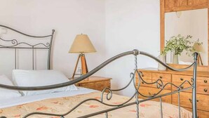 Ein Bett mit Metallgestell, ein Nachttisch mit Lampe, eine Holzkommode und ein Spiegel.