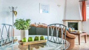Ein Wohnzimmer mit Glastisch, Stühlen, einer Couch, einem Kamin und einem Blumentopf.