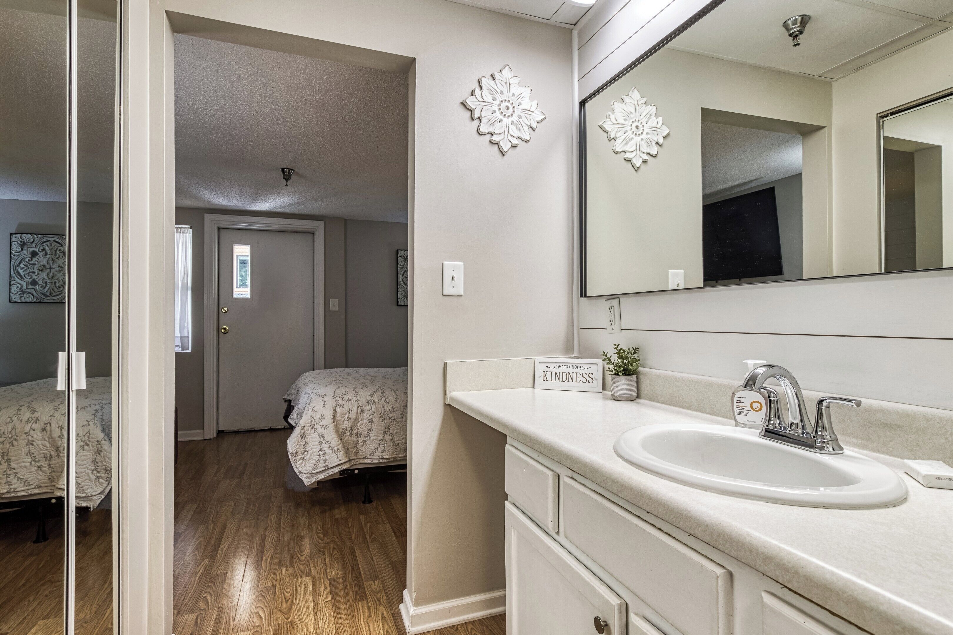 Une chambre avec un lit, une salle de bain avec un lavabo et un miroir, et un couloir.
