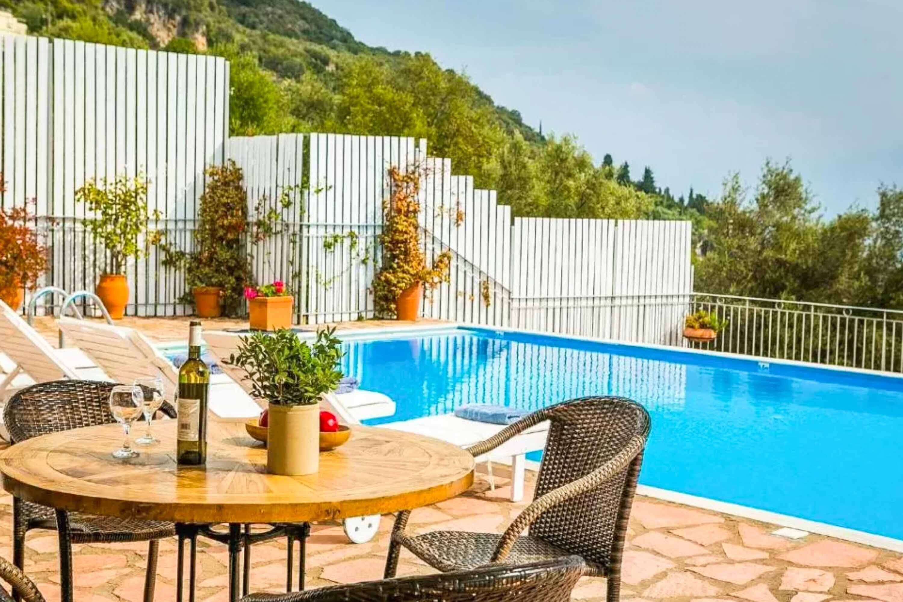 Un espace aménagé au bord de la piscine, avec une table ronde, des chaises en osier et des plantes en pot.