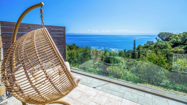 Een rieten stoel op een balkon met uitzicht op zee en begroeiing.