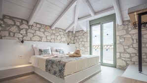 Een slaapkamer met een stenen muur, een bed met een geborduurde spreideken en een uitzicht buiten door een glazen deur.