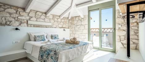 A bedroom with a stone wall, a bed with a patterned bedspread, a wooden bench, and a balcony with a view.