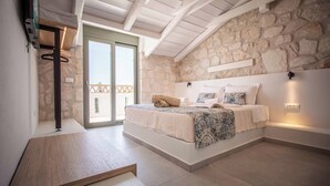 Een slaapkamer met een stenen muur, een bed met beddengoed met een patroon, een houten bank en een schuifdeur naar een balkon.