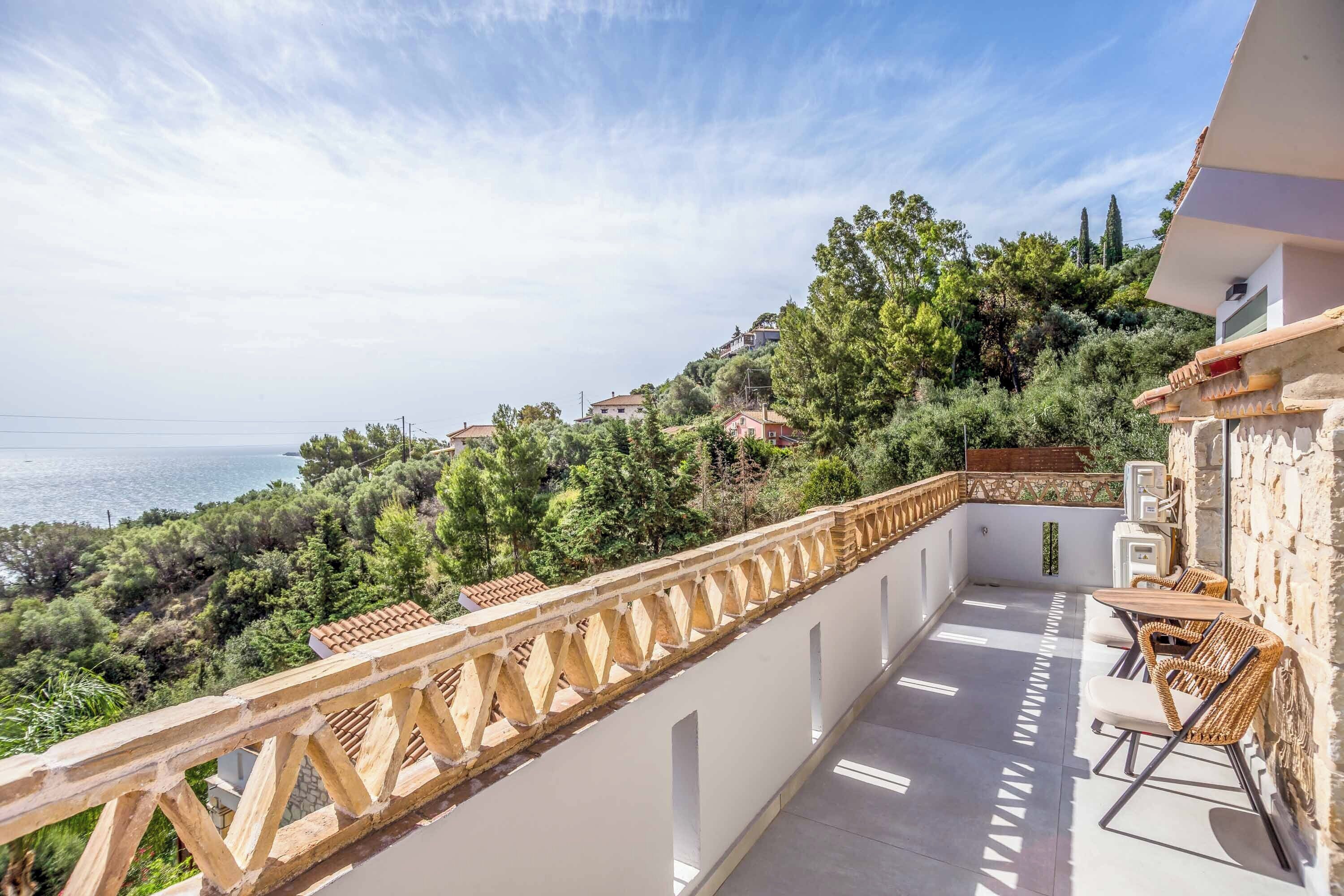 A balcony with a view of the sea and surrounding greenery.