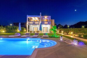 Ein modernes, zweistöckiges Haus mit Swimmingpool, Sitzgelegenheiten im Freien und gut beleuchteten Wegen.
