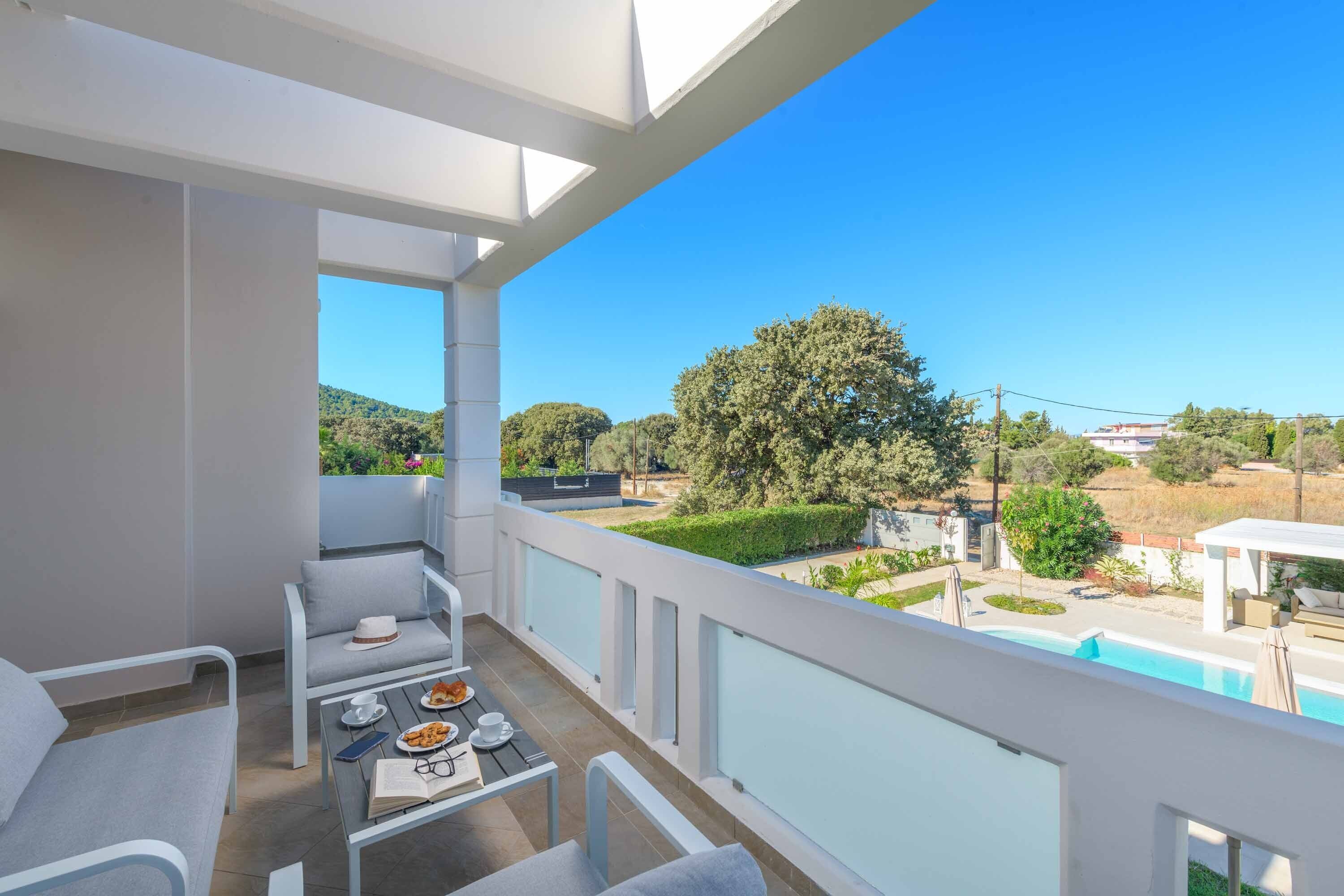 Un balcón con mesa, sillas y vistas a una piscina y follaje.