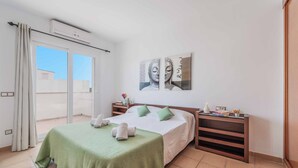 A hotel room with a bed, a nightstand, a bedside table, a wall-mounted air conditioner, and a sliding glass door leading to a balcony.