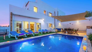 A modern poolside area with a clear pool, lounge chairs, and a dining area.