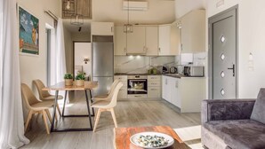 Una cocina moderna con armarios blancos, un comedor con mesa y sillas de madera, y un sofá gris.
