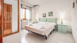 A bedroom with a bed, two bedside tables with lamps, a radiator, and a window with curtains.