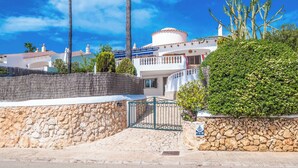A coastal building with a stone wall, a metal gate, and a palm tree.