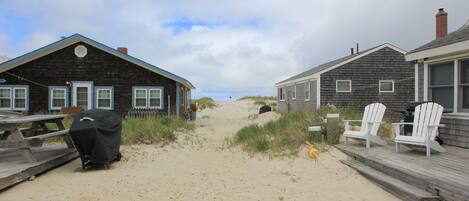A beachside property with wooden houses, a sandy path, and beach chairs.