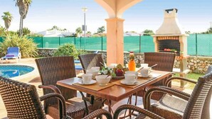 An outdoor patio with wicker furniture, a grill, and a pool in the background.