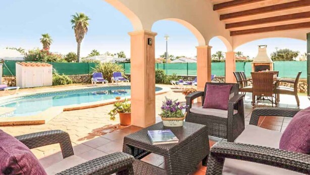 A covered outdoor area with wicker furniture, a pool, and a view of the surrounding landscape.